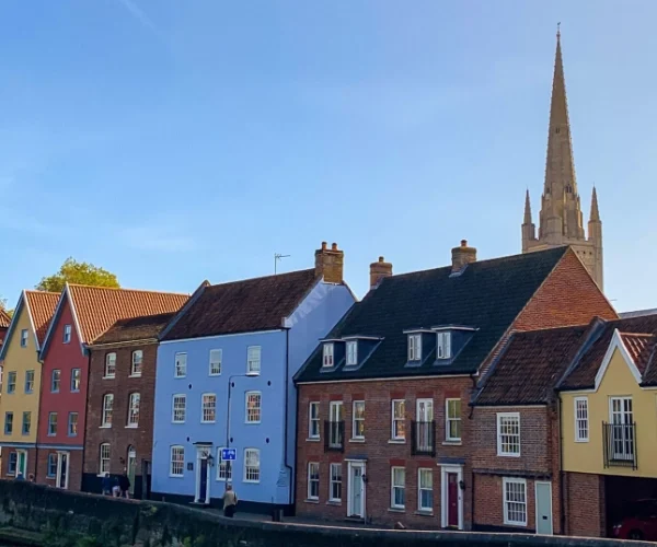 Row of colourful houses with pitched roofs, a tall church spire in the background, and a clear blue sky overhead.